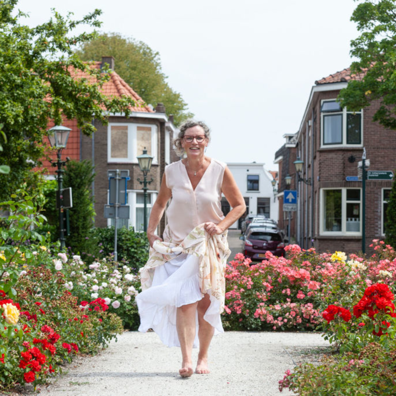 Vrouw in witte kleding loopt langs bloeiende rozen in een tuin.
