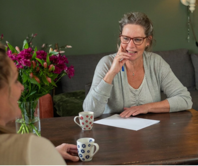 Twee vrouwen in gesprek aan een tafel, waarbij één vrouw luistert.