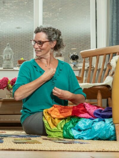 Vrouw zit tussen kleurrijke doeken en werkt met kleur tijdens Innerlijk Kleurenwerk.